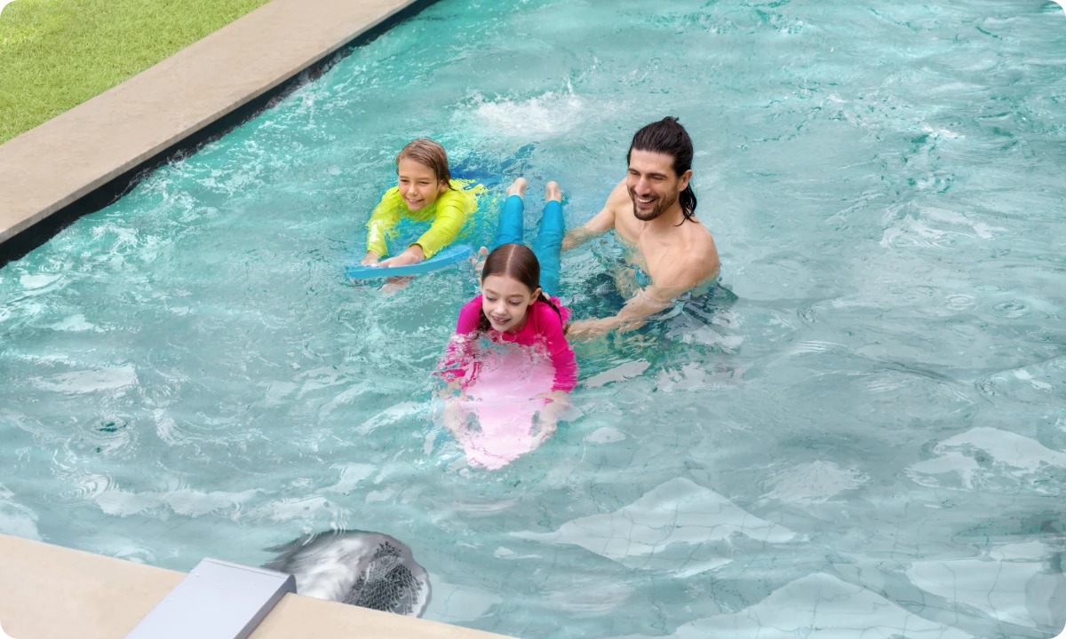 Un père et ses enfants se détendent dans la piscine grâce au courant constant du système iGarden Swim Jet, parfait pour la nage libre.